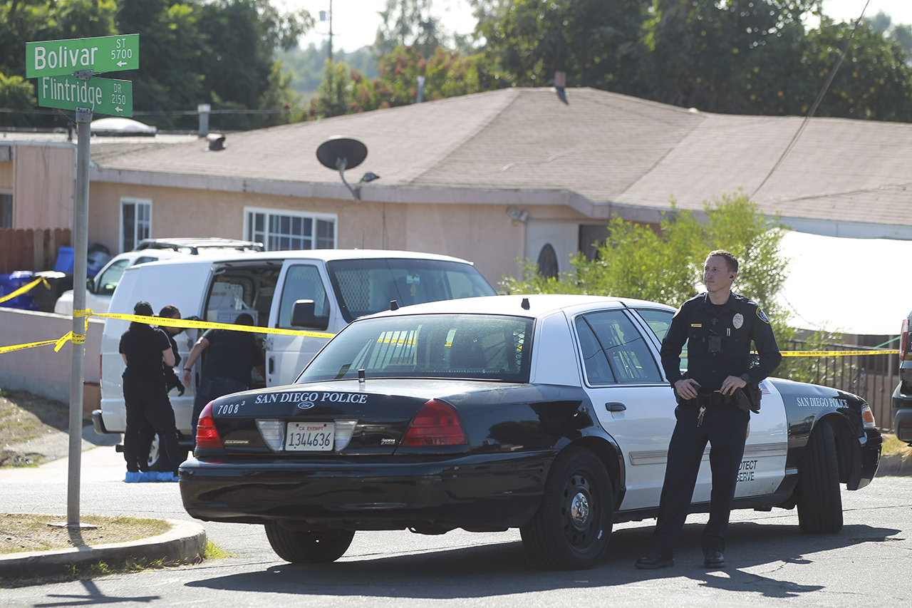 A San Diego Police officer stands in front of a home where two adults and three children died