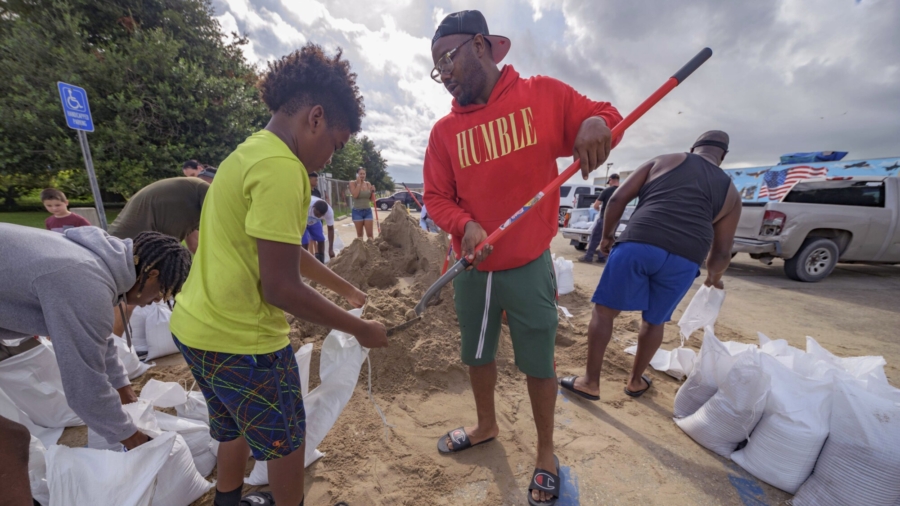 Jawan Williams shovels sand for a sandbag held by his son Jayden Williams, before landfall of Hurricane Ida at the Frederick Sigur Civic Center in Chalmette, La., which is part of the Greater New Orleans metropolitan area, on Aug. 28, 2021. (Matthew Hinton/AP Photo)