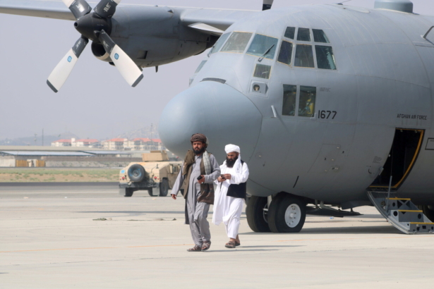 Taliban terrorists walk in front of a military airplane